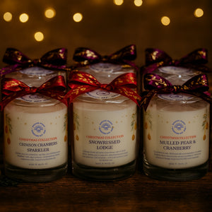 Three candles in glass jars with ribbons on a wooden surface, against a warm, blurred light background.