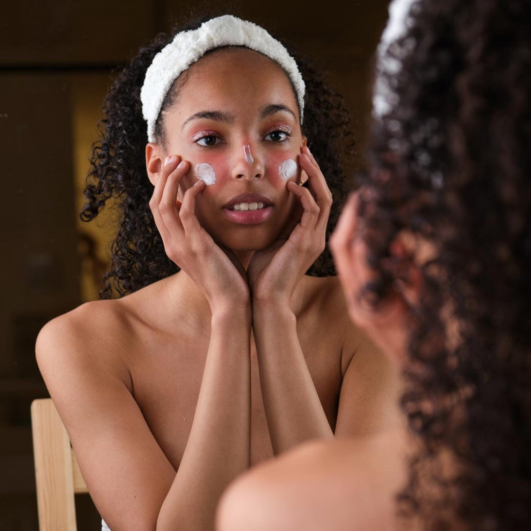 Woman applying cream to her face in front of a mirror